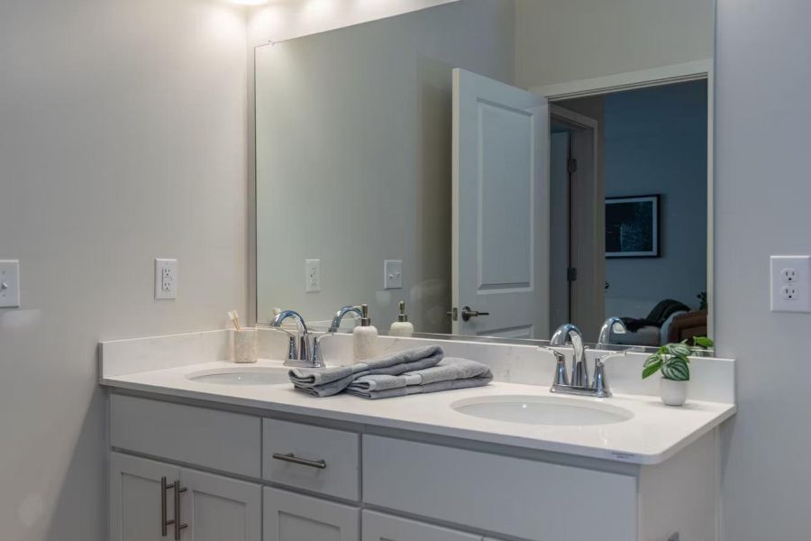 Attain on 5th apartment homes with Modern bathroom vanity with double sinks, large mirror, and overhead lights, featuring white cabinets.