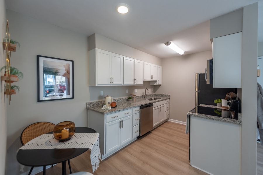 Attain on 5th apartment homes with Modern kitchen with white cabinets, granite countertops, stainless steel appliances, and a small round dining table with two chairs.