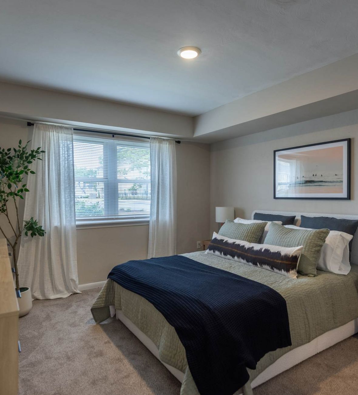 Attain at Chic's Beach  apartment homes with Modern bedroom with a neatly made bed, large window, plants, and neutral decor.