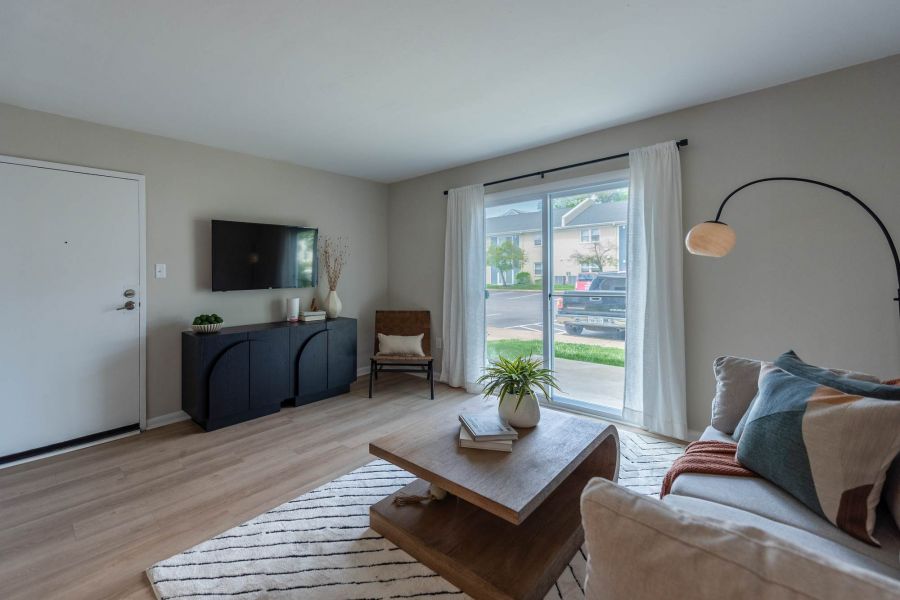 Attain at Chic's Beach homes with Modern living room with a sofa, coffee table, TV, and large window letting in natural light.