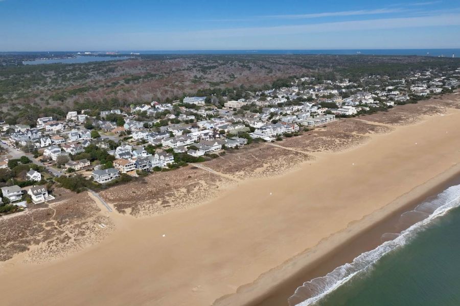Attain at Chic's Beach with Aerial view of a sandy beach, ocean waves, and a coastal town with many houses and greenery.