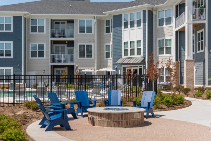 Attain at Chic's Beach homes with Blue chairs surround a fire pit in a courtyard, with a pool and apartment building in the background.