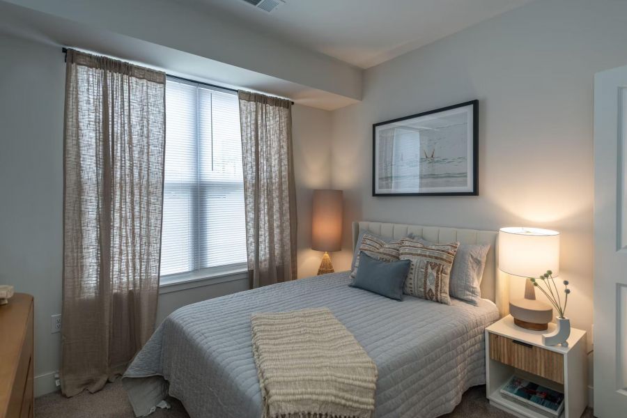 Attain on 5th apartment homes with Cozy bedroom with a neatly made bed, two lamps, framed art above the bed, and sheer curtains on the window.