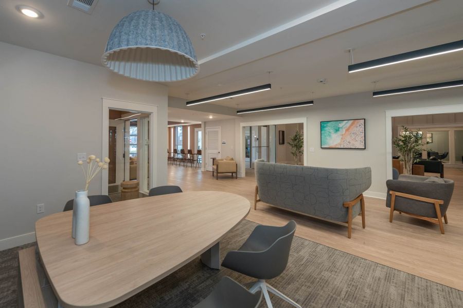 Attain at Chic's Beach homes with Modern lounge with light wood floors, gray sofas, a table with chairs, and a large hanging lamp.