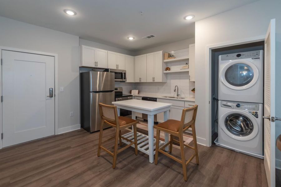 Attain on 5th apartment homes with Modern kitchen with white cabinets, stainless appliances, island with chairs, and stacked washer and dryer.