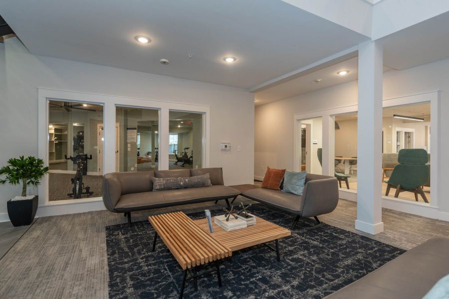 Attain at Chic's Beach homes with Modern lounge area with gray sofas, a wooden coffee table, and large windows overlooking a gym and meeting space.