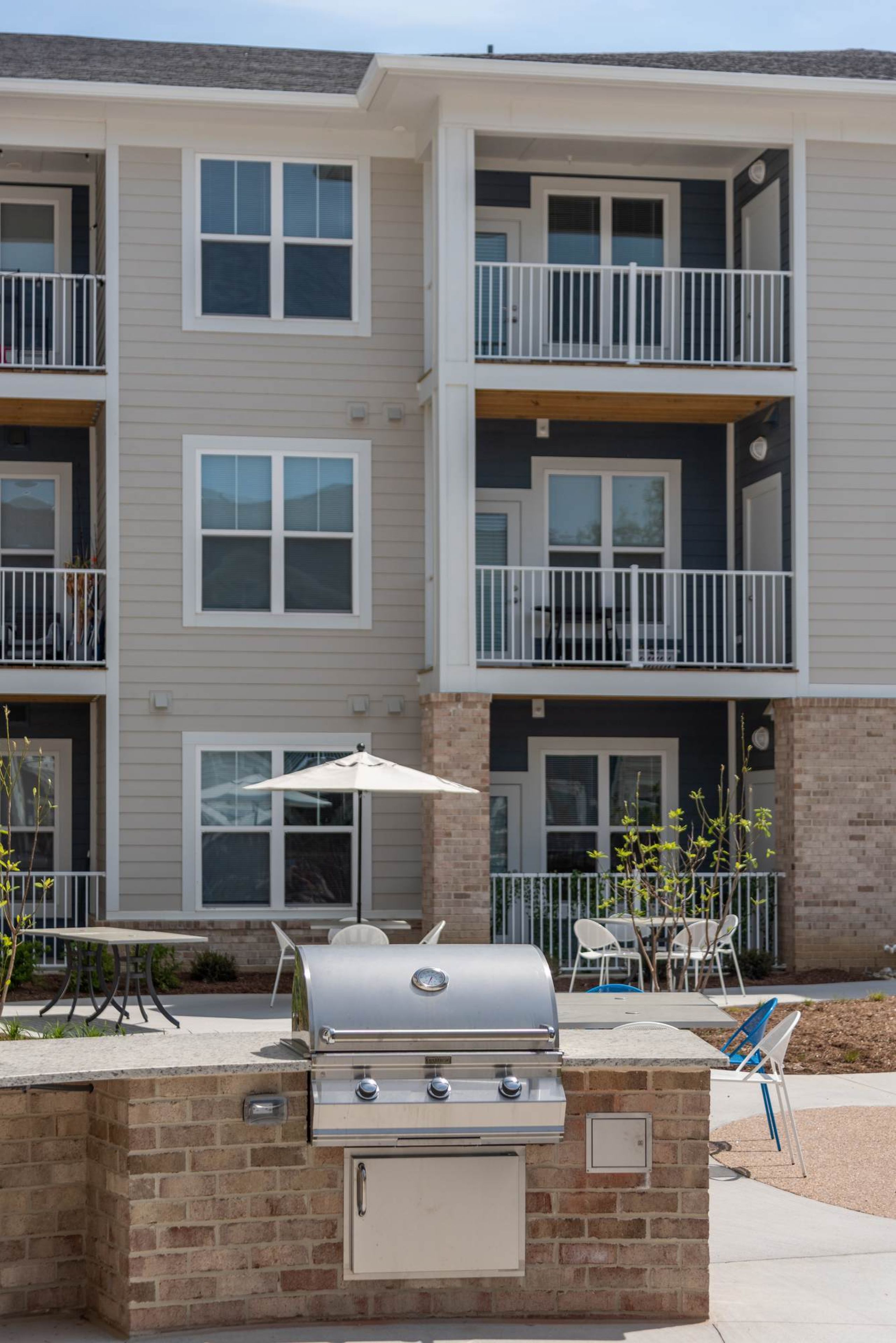 Attain at Chic's Beach apartment homes with Outdoor grill in front of a modern apartment building with balconies and patio furniture.