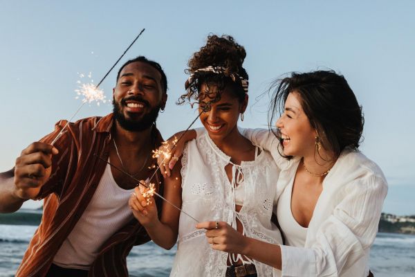 Attain on 5th apartment homes with Three friends smiling and holding sparklers together on a beach at sunset.