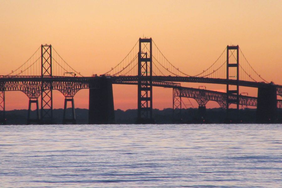 Attain at Chic's Beach with A suspension bridge silhouetted against an orange sunset sky over calm water.