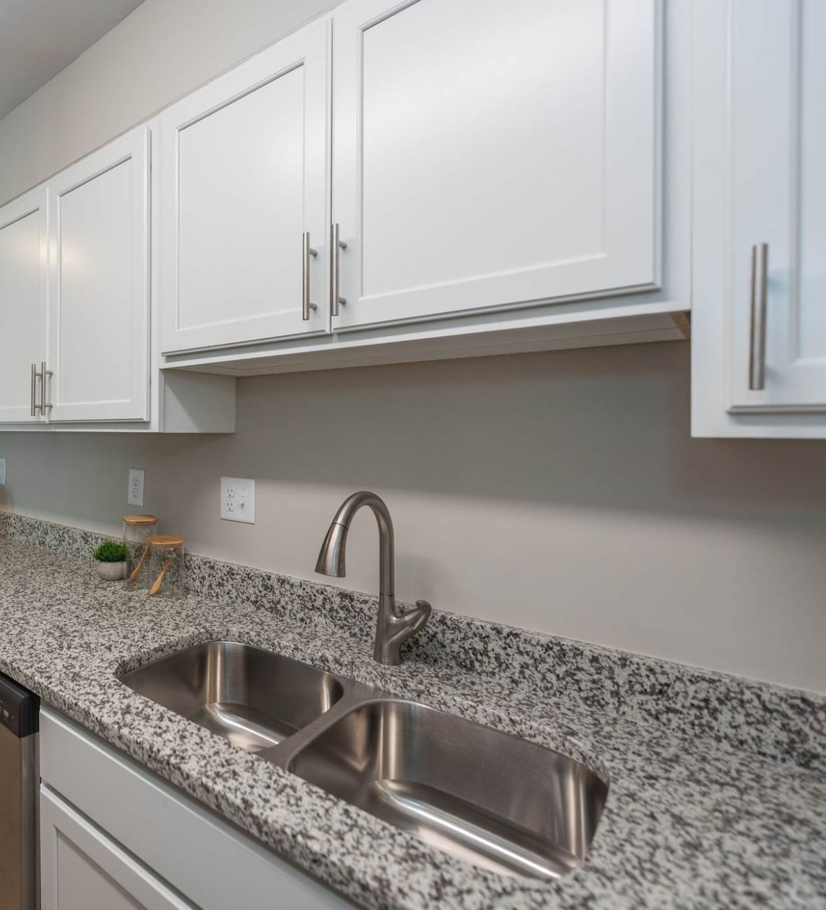 Attain at Chic's Beach  apartment homes with Modern kitchen with granite countertops, white cabinets, double sink, and a small dining area with two chairs.
