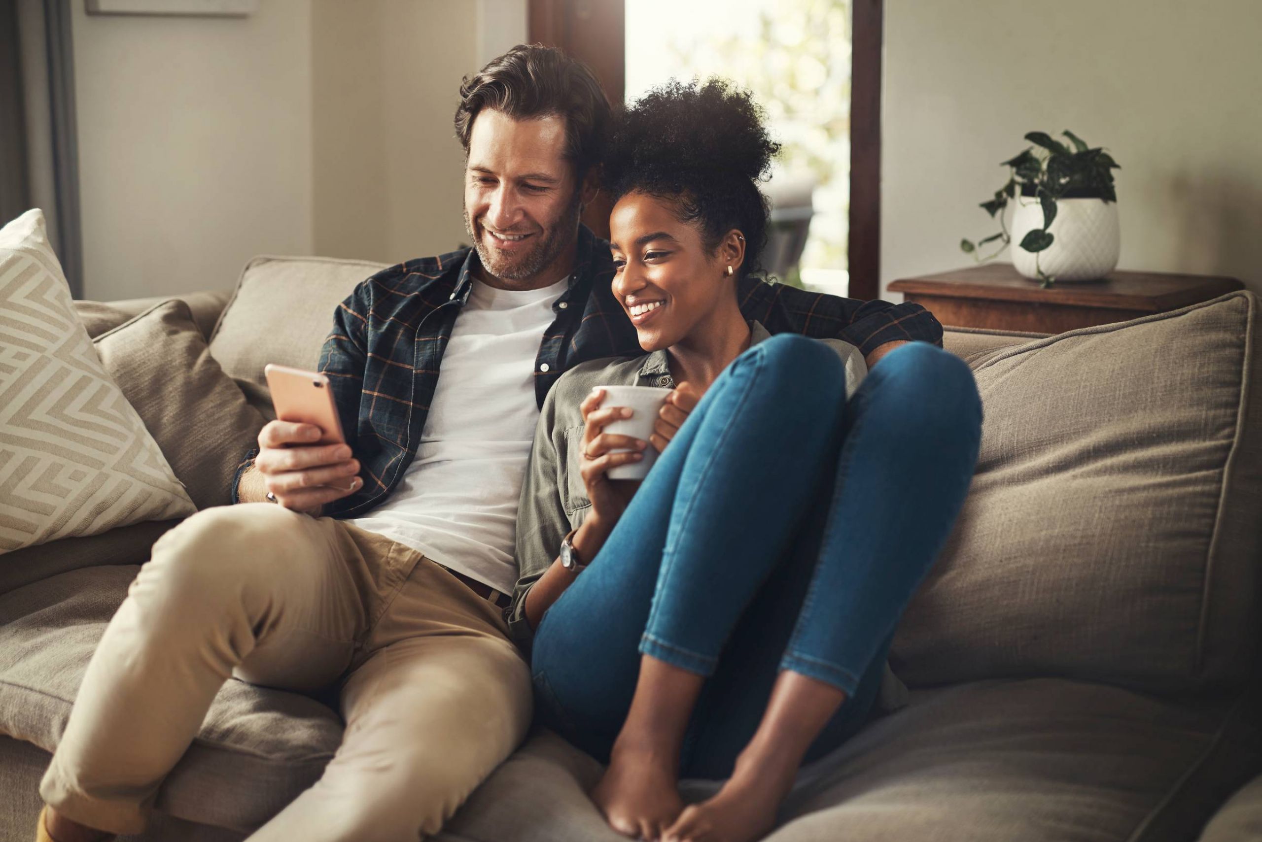 Attain on 5th apartment homes with A smiling couple sits on a couch, looking at a smartphone together and holding a mug.
